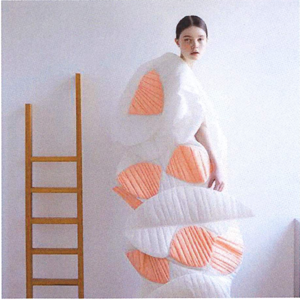 Lady dressed in unconventional poofy, white and orange dress, stood next to a ladder.